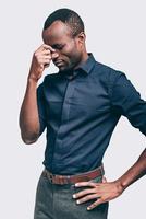 känsla så trött. frustrerad ung afrikansk man masse näsa och förvaring ögon stängd medan stående mot grå bakgrund foto