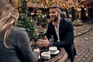 delning bra idéer. stilig ung man i smart tillfällig ha på sig leende medan har en konversation med ung kvinna i restaurang utomhus foto