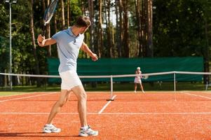 praktiserande med vän. full längd av man och kvinna spelar tennis på tennis domstol foto