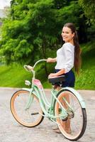 redo för en rida. attraktiv ung leende kvinna gående med henne årgång cykel och ser på kamera foto