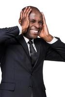 betonade affärsman. deprimerad ung afrikansk man i formell klädsel innehav huvud i händer och grimaserande medan stående isolerat på vit bakgrund foto