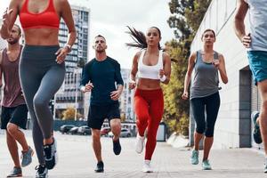 grupp av ung människor i sporter Kläder joggning medan utövar på de trottoar utomhus foto