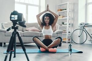 skön ung afrikansk kvinna Sammanträde i de yoga medan framställning social media video foto