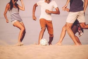 strand boll med vänner. beskurna bild av ung människor spelar med fotboll boll på de strand foto
