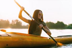 perfekt dag för Kajakpaddling. skön ung leende kvinna paddling medan Sammanträde i kajak foto