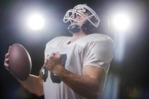 Begagnade till vinna. porträtt av amerikan fotboll spelare innehav boll och skrikande medan stående mot lampor foto