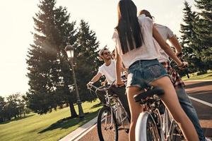 bara utgifterna tid med vänner. grupp av Lycklig ung människor i tillfällig ha på sig leende medan cykling tillsammans utomhus foto