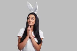omtänksam kanin. attraktiv ung kvinna i kanin öron ser bort och leende medan stående mot grå bakgrund foto