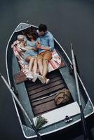 stunder av intimitet. topp se av skön ung kvinna läsning bok medan Sammanträde i de båt med henne pojkvän foto