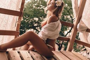 sorglös och avslappnad. attraktiv ung kvinna i badkläder avkopplande medan Sammanträde i de träd hus utomhus foto