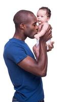 jag kärlek min bebis. ung afrikansk man innehav hans liten bebis och kissing honom medan stående isolerat på vit foto