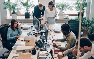 grupp av ung modern människor i smart tillfällig ha på sig kommunicerar och använder sig av modern teknik medan arbetssätt i de kontor foto