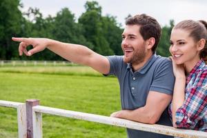 ranch roligt. sida se av Lycklig ung kärleksfull par stående stänga till varje Övrig och leende medan man pekande bort foto