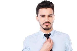 självsäker och framgångsrik. självsäker ung man i skjorta och slips ser på kamera och justeras hans slips medan stående mot vit bakgrund foto