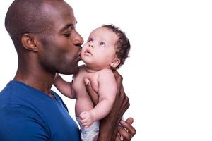 far och bebis. ung afrikansk man innehav hans liten bebis och kissing honom medan stående isolerat på vit foto