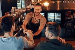 topp se av bartender tjänande öl till ung män medan stående på de bar disken i pub foto