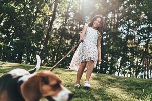 vänner evigt. full längd av söt liten flicka spelar med henne hund medan gående utomhus foto