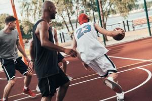 snabbt som en smal. grupp av ung män i sporter Kläder spelar basketboll medan utgifterna tid utomhus foto