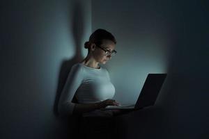 skön ung kvinna arbetssätt på bärbar dator mot en mörk vägg foto