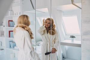 attraktiv ung kvinna i morgonrock ser på henne reflexion i de spegel foto