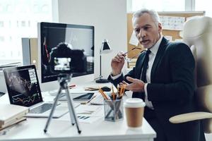 senior man i elegant företag kostym använder sig av modern teknik medan framställning social media video foto