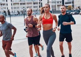 grupp av ung människor i sporter Kläder joggning medan utövar på de trottoar utomhus foto