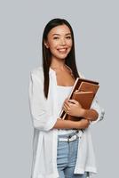intelligens. skön ung asiatisk kvinna bärande böcker och leende medan stående mot grå bakgrund foto