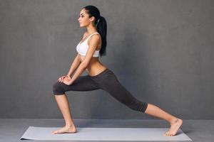 krigare. sida se av skön ung afrikansk kvinna i sportkläder praktiserande yoga på övning matta mot grå bakgrund foto