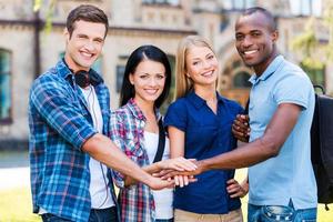 de bäst vänner någonsin. fyra Lycklig ung människor innehav deras händer tillsammans och leende medan stående utomhus foto