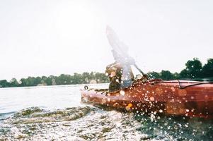 njuter flod äventyr. ung man stänk vatten medan Kajakpaddling på flod foto