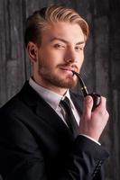elegans och manlighet. porträtt av stilig ung man i formell klädsel rökning en rör och leende på kamera foto