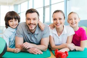 Lycklig familj i kondition klubb. Lycklig sportig familj bindning till varje Övrig medan liggande på övning matta tillsammans foto