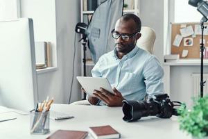 stilig ung afrikansk man använder sig av digital läsplatta medan arbetssätt i de modern kontor foto