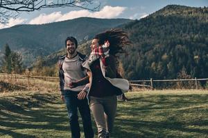 kärlek inspirerar dem. Lycklig ung par leende medan löpning på de dal i bergen utomhus foto