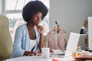 skön ung afrikansk kvinna använder sig av bärbar dator medan arbetssätt i design studio foto