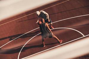 likvärdig motståndare. topp se av ung män i sporter Kläder spelar basketboll medan utgifterna tid utomhus foto