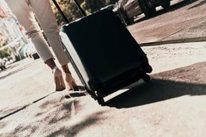 företag resa. stänga upp bak- se av ung kvinna dragande bagage medan gående utomhus foto