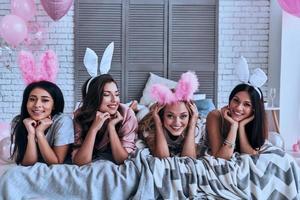 rolig kaniner. fyra lekfull ung kvinnor i kanin öron leende medan liggande på de säng foto
