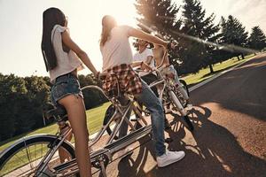 perfekt dag för en cykel rida. grupp av Lycklig ung människor i tillfällig ha på sig leende medan cykling tillsammans utomhus foto