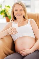 gravid kvinna dricka mjölk. skön gravid kvinna Sammanträde på de stol och innehav glas av mjölk foto