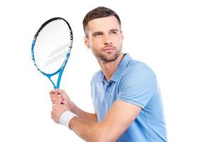 självsäker spelare. självsäker ung man innehav tennis racket och ser koncentrerad medan stående mot vit bakgrund foto