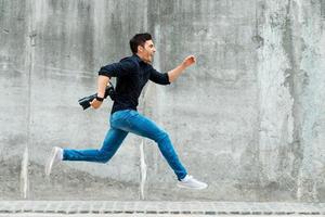 skyndar till vara först. full längd av ung fotograf löpning mot en betong vägg foto