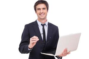 självsäker företag expert. glad ung man i formell klädsel innehav bärbar dator och leende medan stående isolerat på vit bakgrund foto