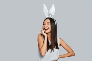 sötare än några kanin. skön ung asiatisk kvinna i kanin öron leende medan stående mot grå bakgrund foto