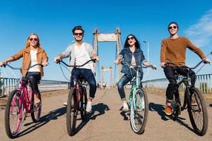 vi kärlek ridning tillsammans. full längd av fyra ung människor ridning deras cyklar och leende foto