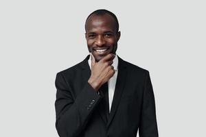 eleganta ung afrikansk man i formell klädsel ser på kamera och leende medan stående mot grå bakgrund foto