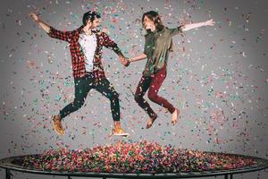 de kärlek har roligt. i luften skott av skön ung glad par innehav händer medan Hoppar på trampolin tillsammans med konfetti Allt runt om dem foto