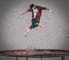 sorglös roligt. i luften skott av stilig ung man Hoppar på trampolin med konfetti Allt runt om honom foto