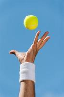 tjänande tennis boll. närbild av manlig hand i handledsband kasta tennis boll mot blå himmel foto