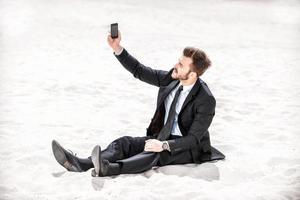 fattig signal. frustrerad ung affärsman sökande för mobil telefon signal medan Sammanträde på sand i öken- foto